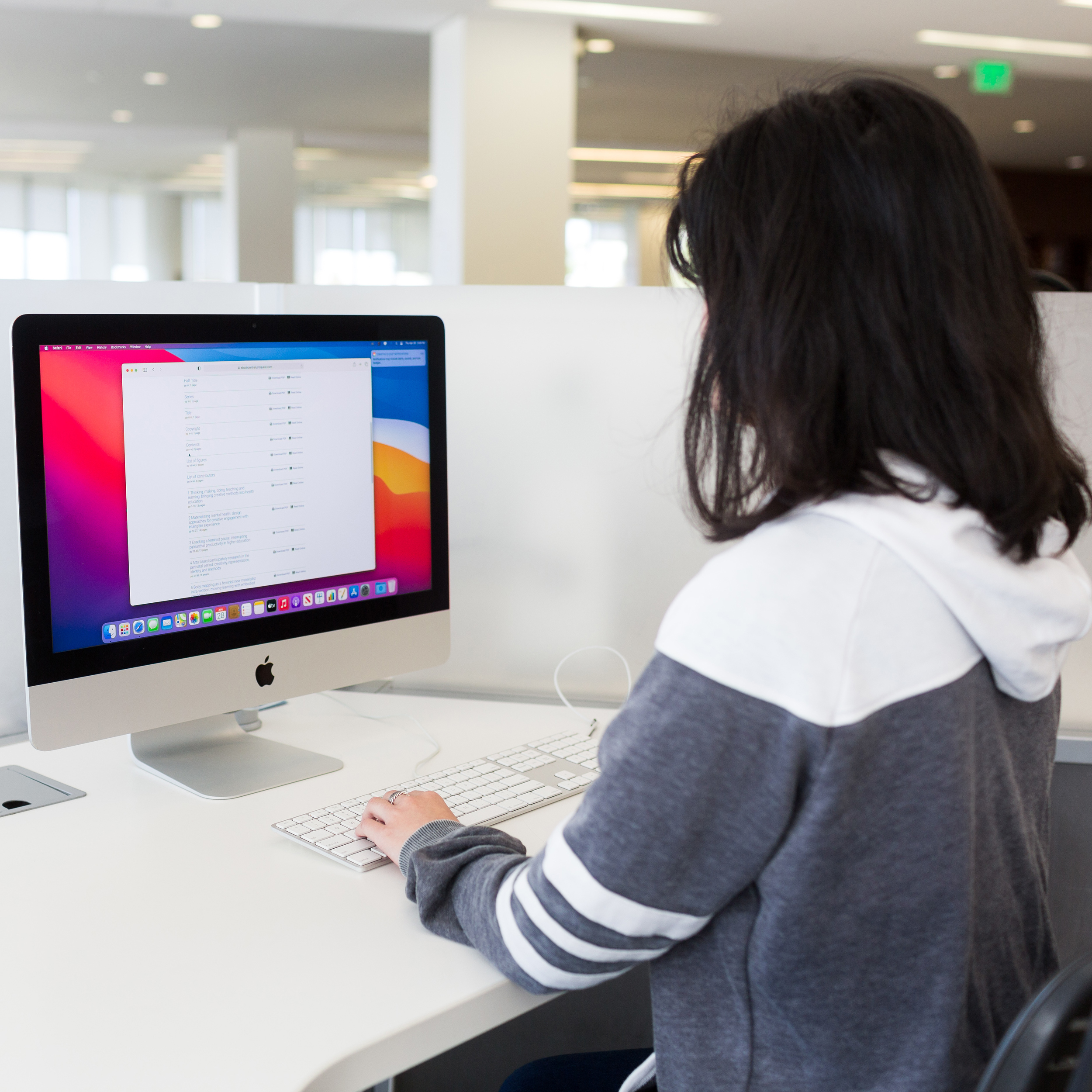 a student's back to the camera as they navigate on an iMac